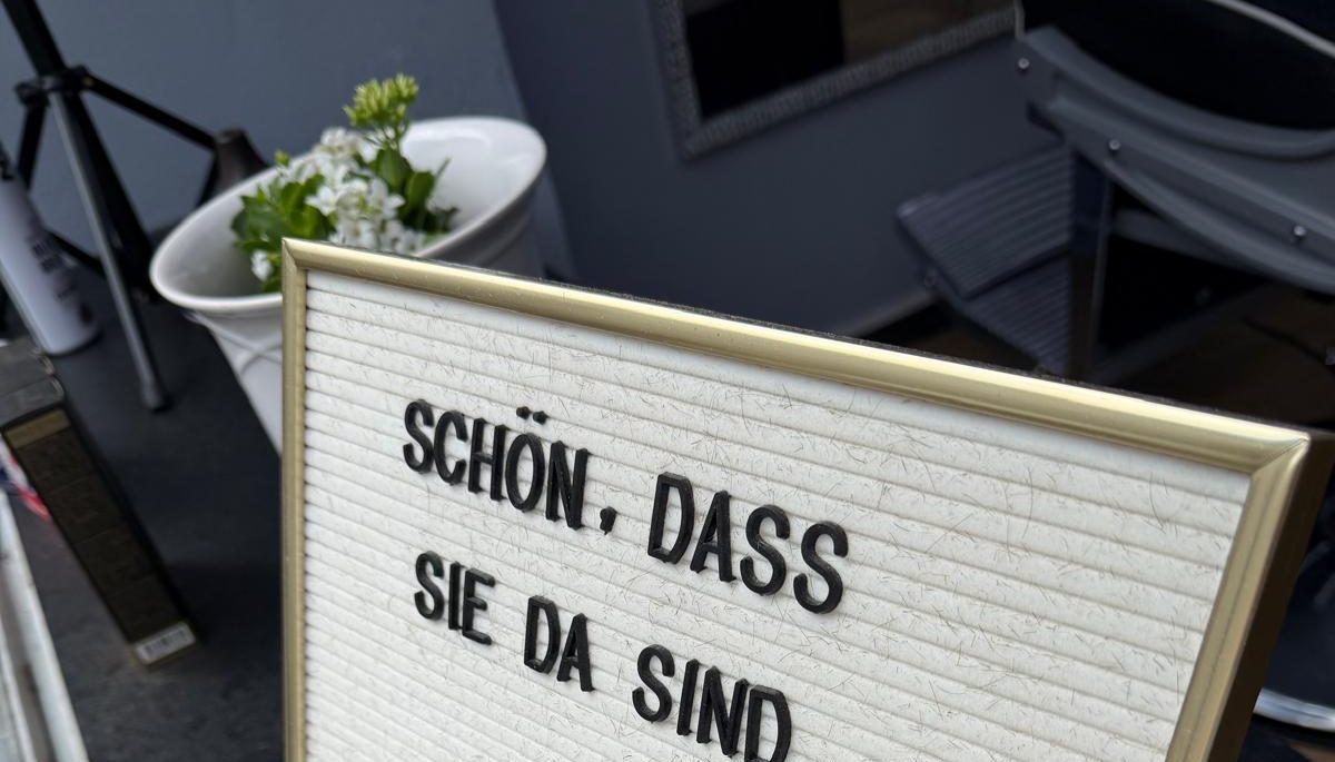 Letterboard mit goldenem Rahmen vor dem Salon: Schön, dass Sie da sind
